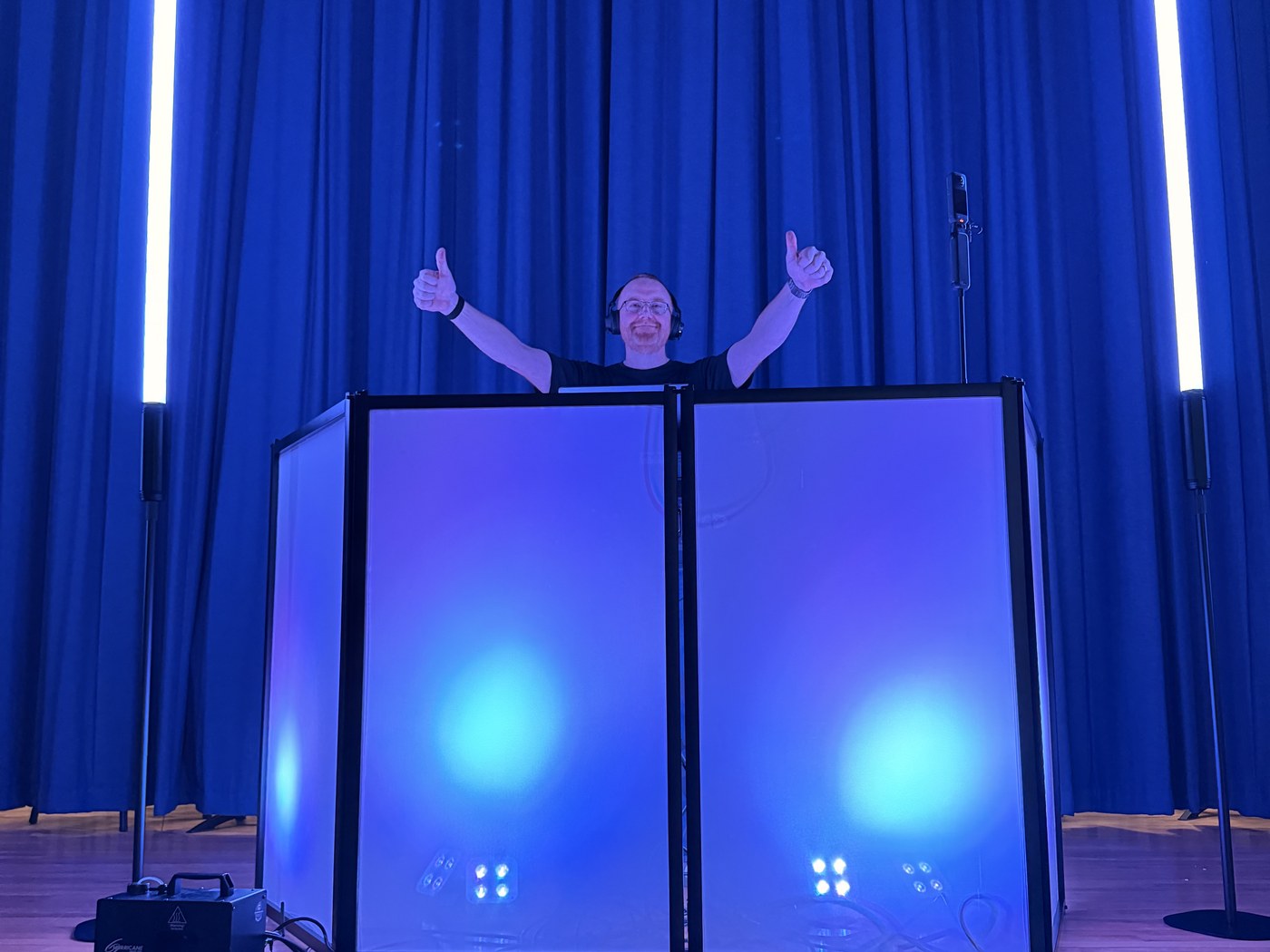 James behind a school-event DJ setup, acknowledging the crowd