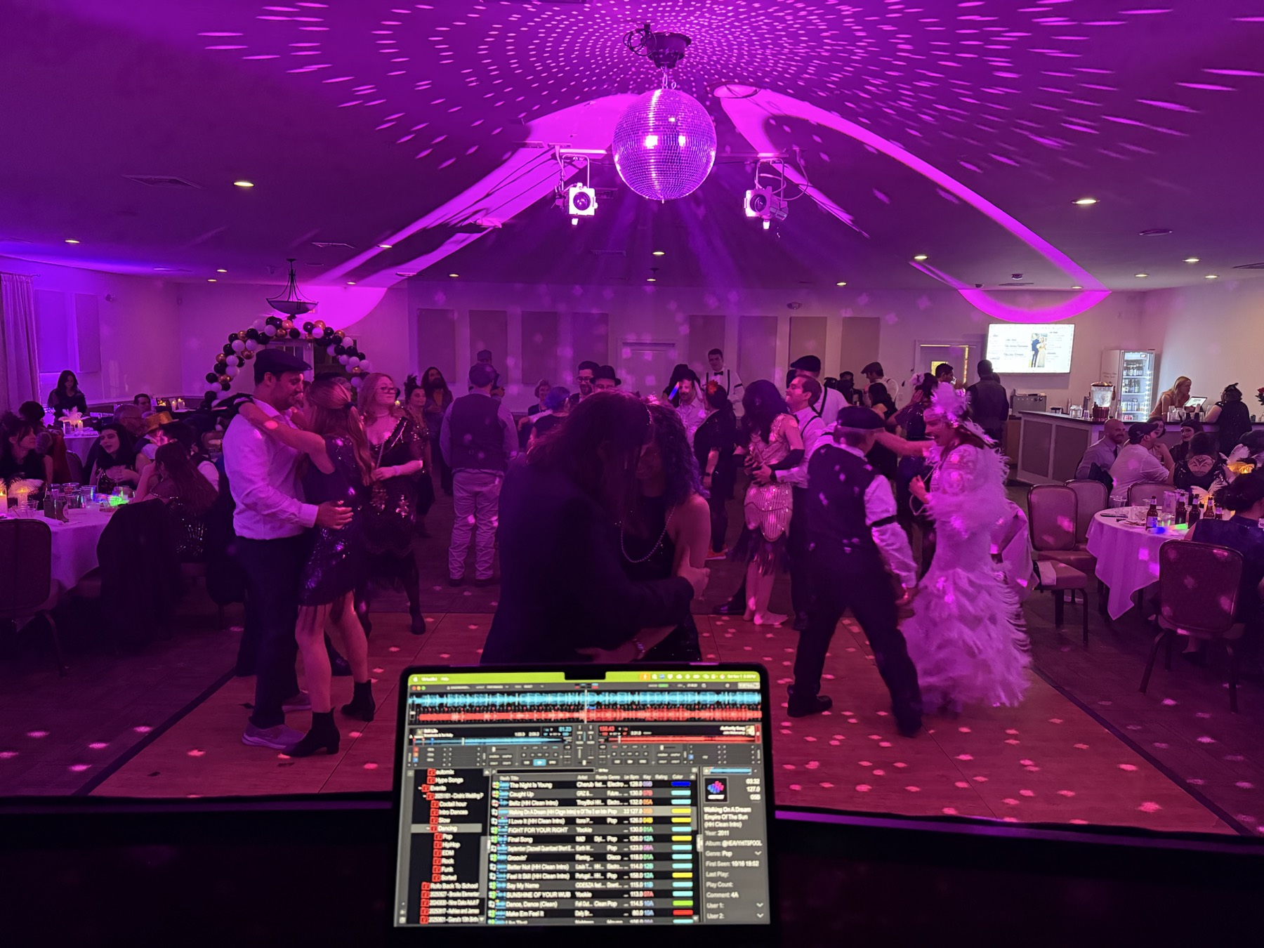 A packed celebration dance floor beneath a disco ball and vivid pink lighting